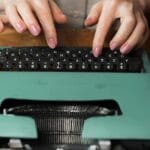 Close-up of hands typing on a retro green typewriter indoors, highlighting vintage writing tools.