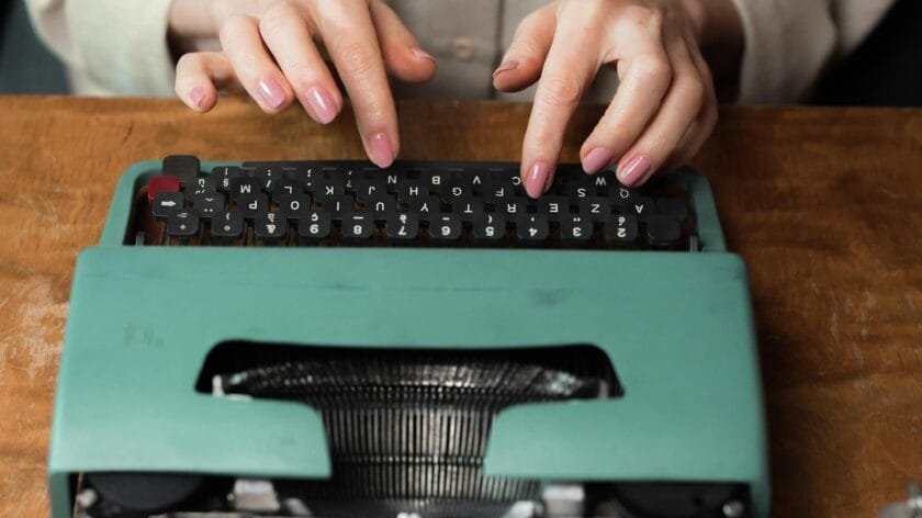 Close-up of hands typing on a retro green typewriter indoors, highlighting vintage writing tools.