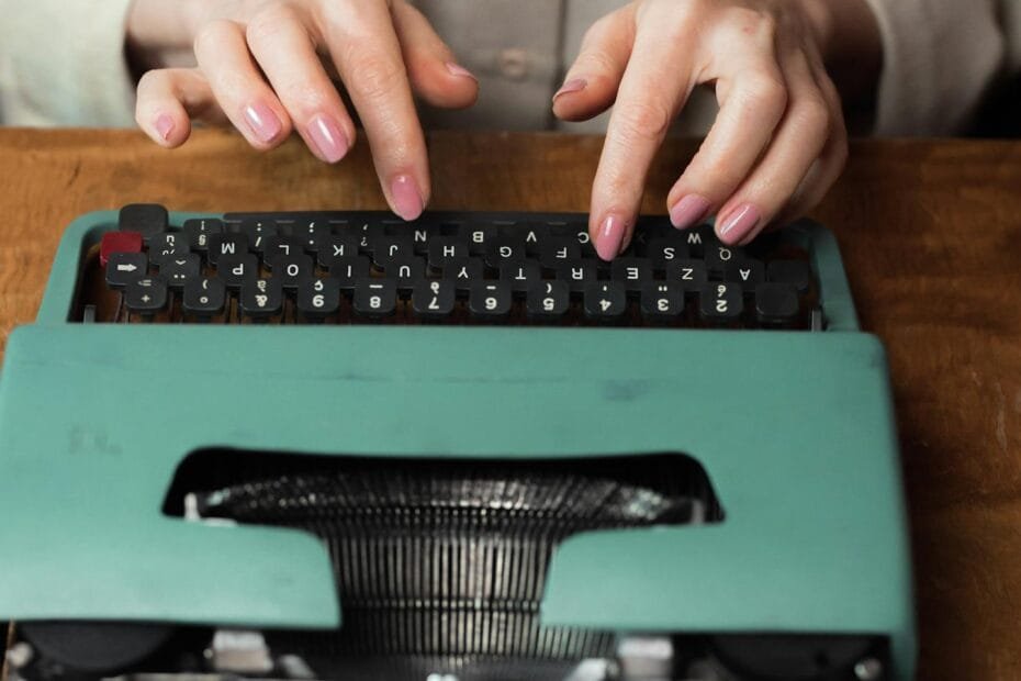 Close-up of hands typing on a retro green typewriter indoors, highlighting vintage writing tools.