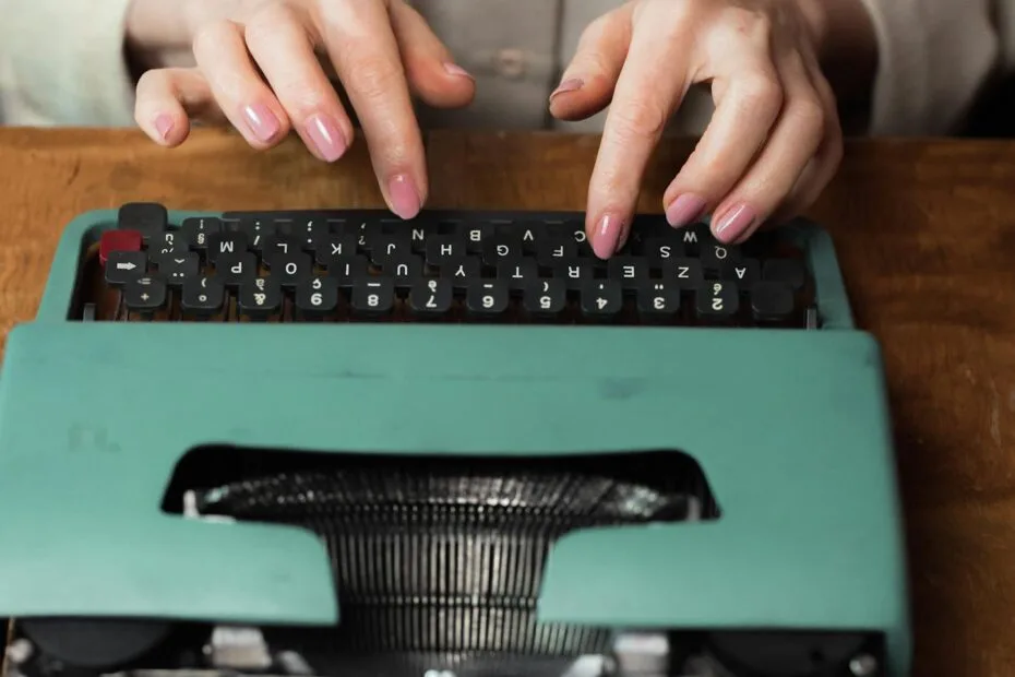 Close-up of hands typing on a retro green typewriter indoors, highlighting vintage writing tools.